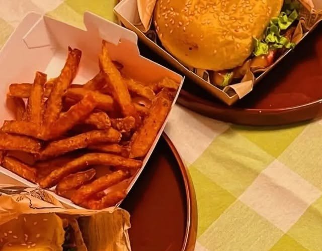 Caixa de batata-doce frita ao lado de hambúrgueres numa mesa com toalha aos quadrados