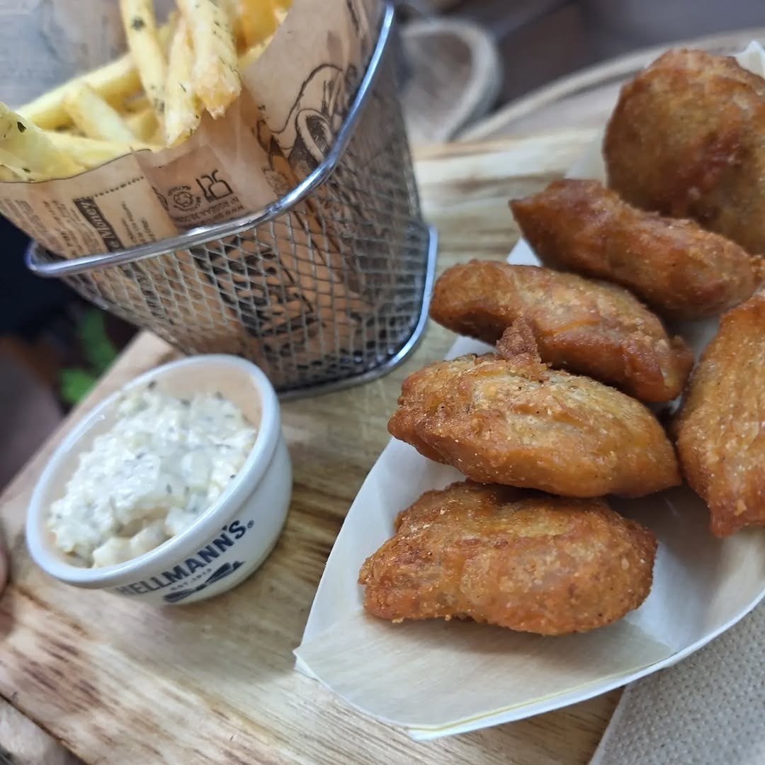 Batatas fritas num cesto, taça de molho e panados dourados sobre tábua de madeira