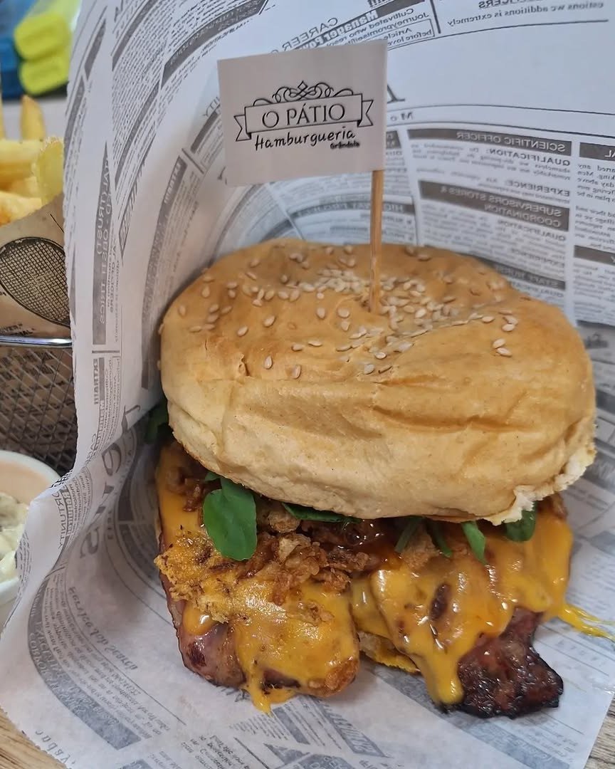 Hambúrguer com cheddar derretido e rúcula, embrulhado em papel de jornal, com a bandeirola da casa